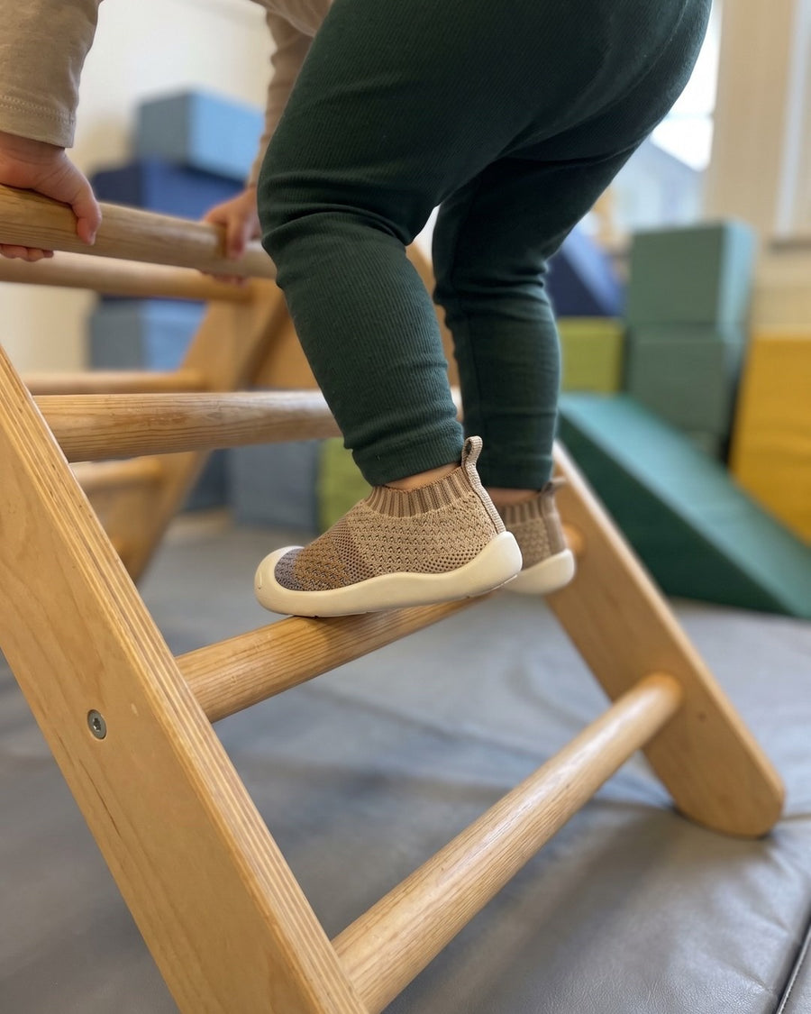 Barn i gröna leggings klättrar i en klätterställning av trä på förskolan, i Upptäckaren ljusbeige