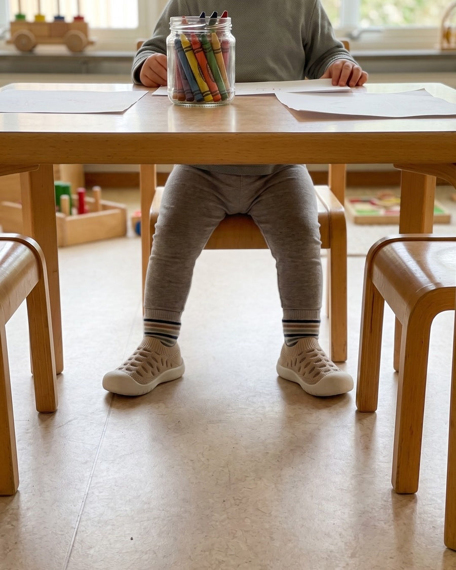 Barn vid ett lågt förskolebord med kritor i en glasburk, randiga strumpor och Drömmaren beige