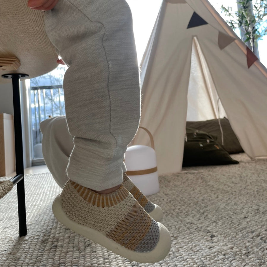 Barn på en stol med foten lyft över en ullmatta framför ett tipitält vid fönstret, i Skaparen beige